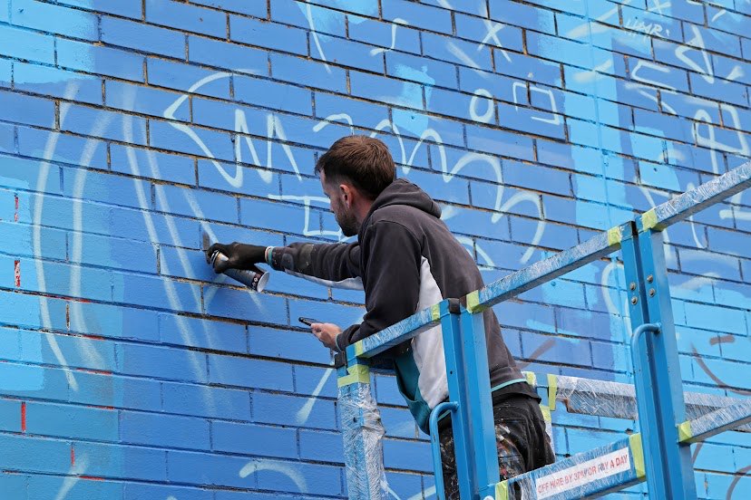 Artist sketching the PushPull mural on a blue wall